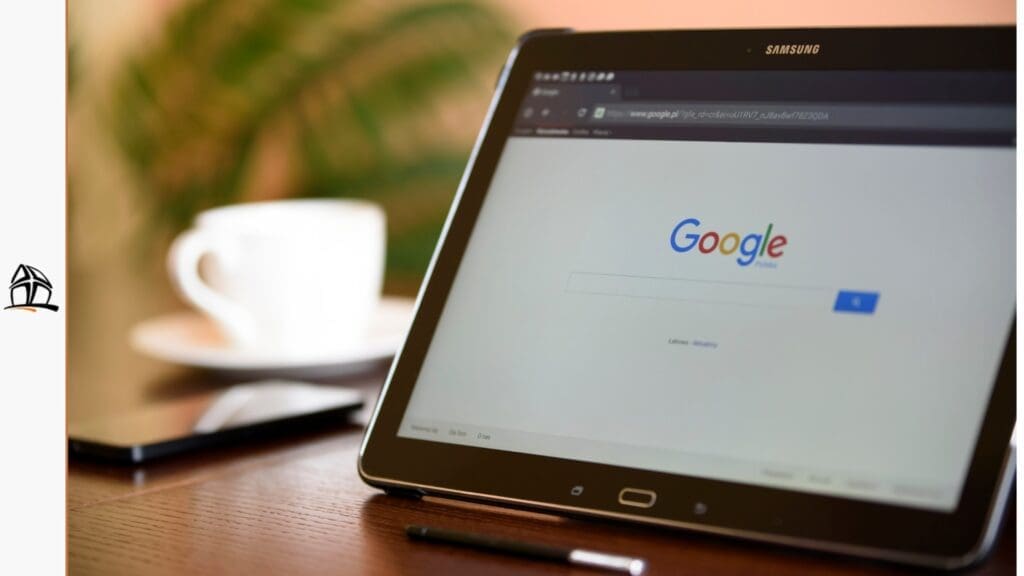 Um tablet Samsung sobre uma mesa de madeira exibindo a página inicial de buscas do Google. Ao fundo, uma xícara de café desfocada.