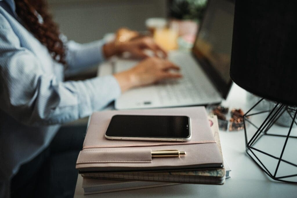 Notebook, agenda e celular sobre uma mesa durante trabalho administrativo. A simulação deve usar documentos de compras e vendas, e não apenas a alíquota aparente.